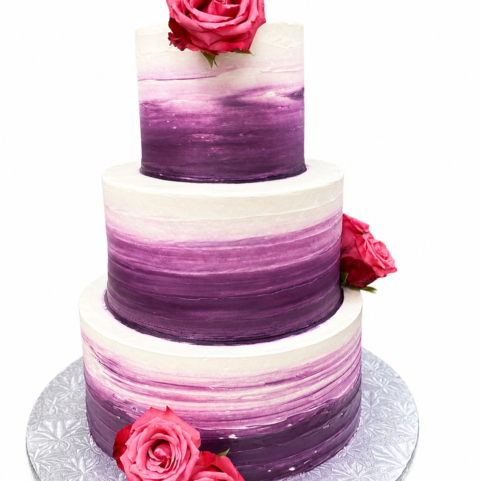Three-tier purple ombré cake decorated with pink roses on an embossed silver cake board.