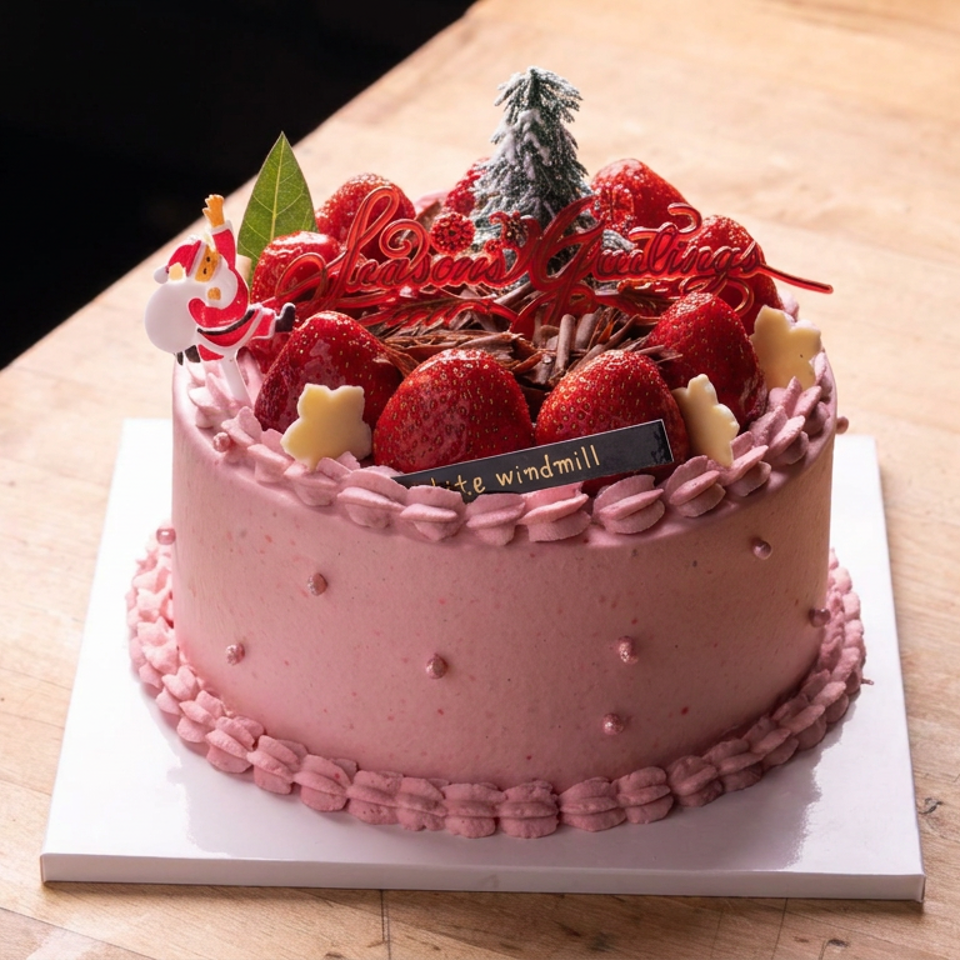 Pink frosted celebration cake topped with strawberries, chocolate shavings, decorative greenery, and a festive greeting on a wooden table.
