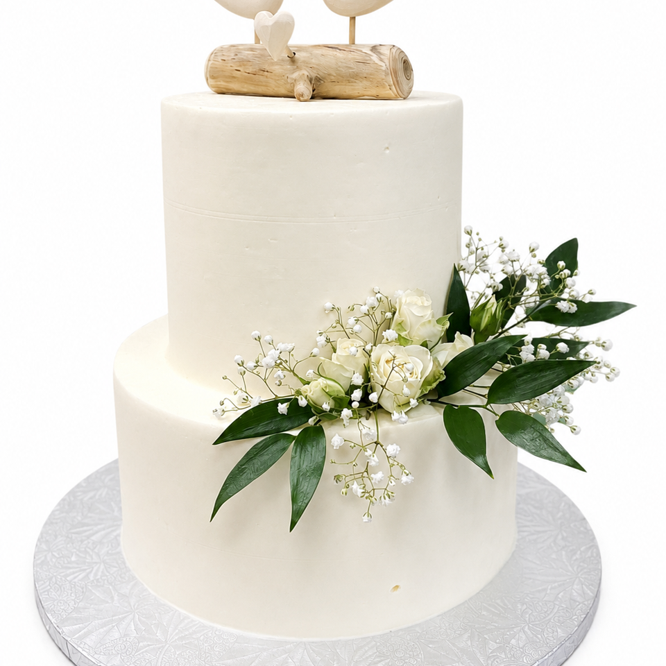 Two-tier white wedding cake decorated with cream roses, baby's breath, greenery, and a wooden dove topper.