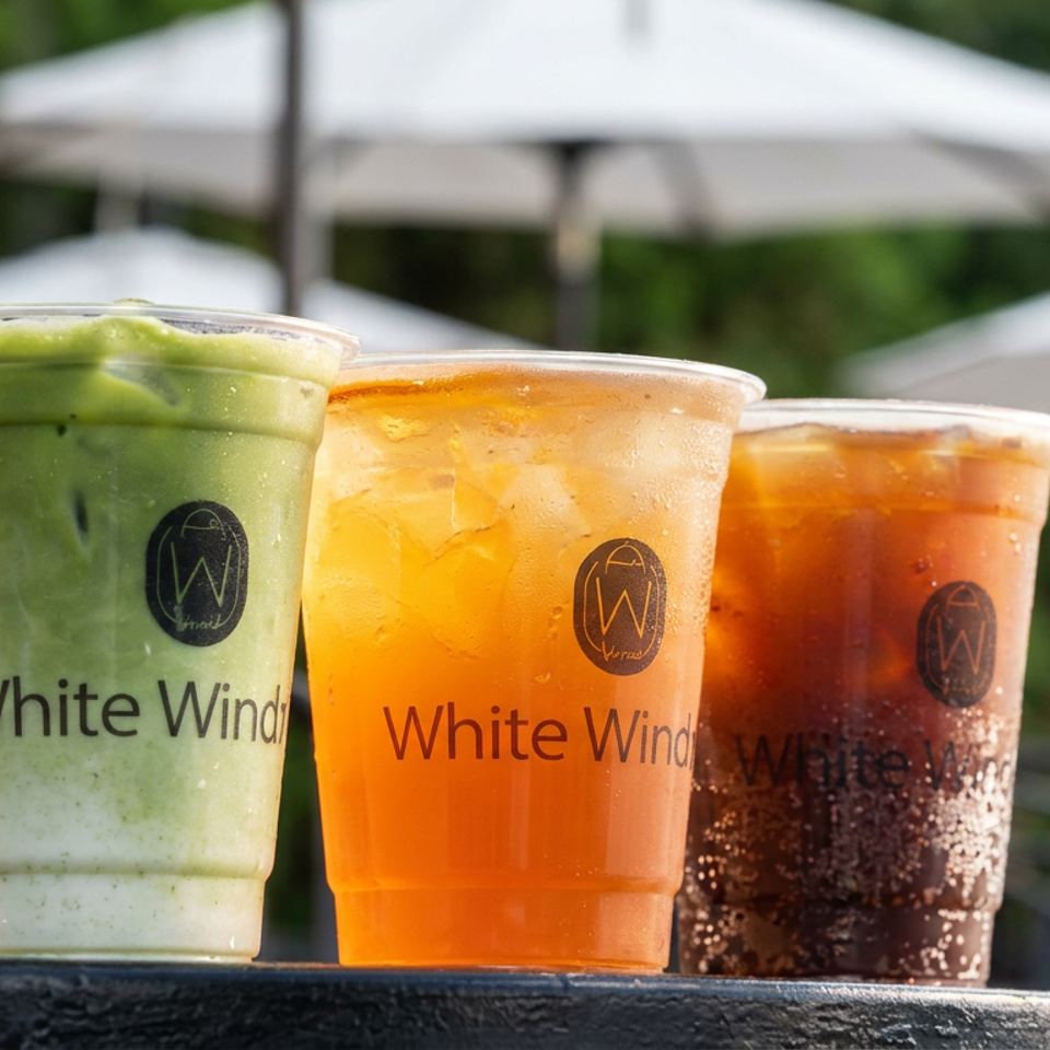 Three White Wind iced drinks: green matcha, orange tea, and dark beverage, with outdoor umbrellas.