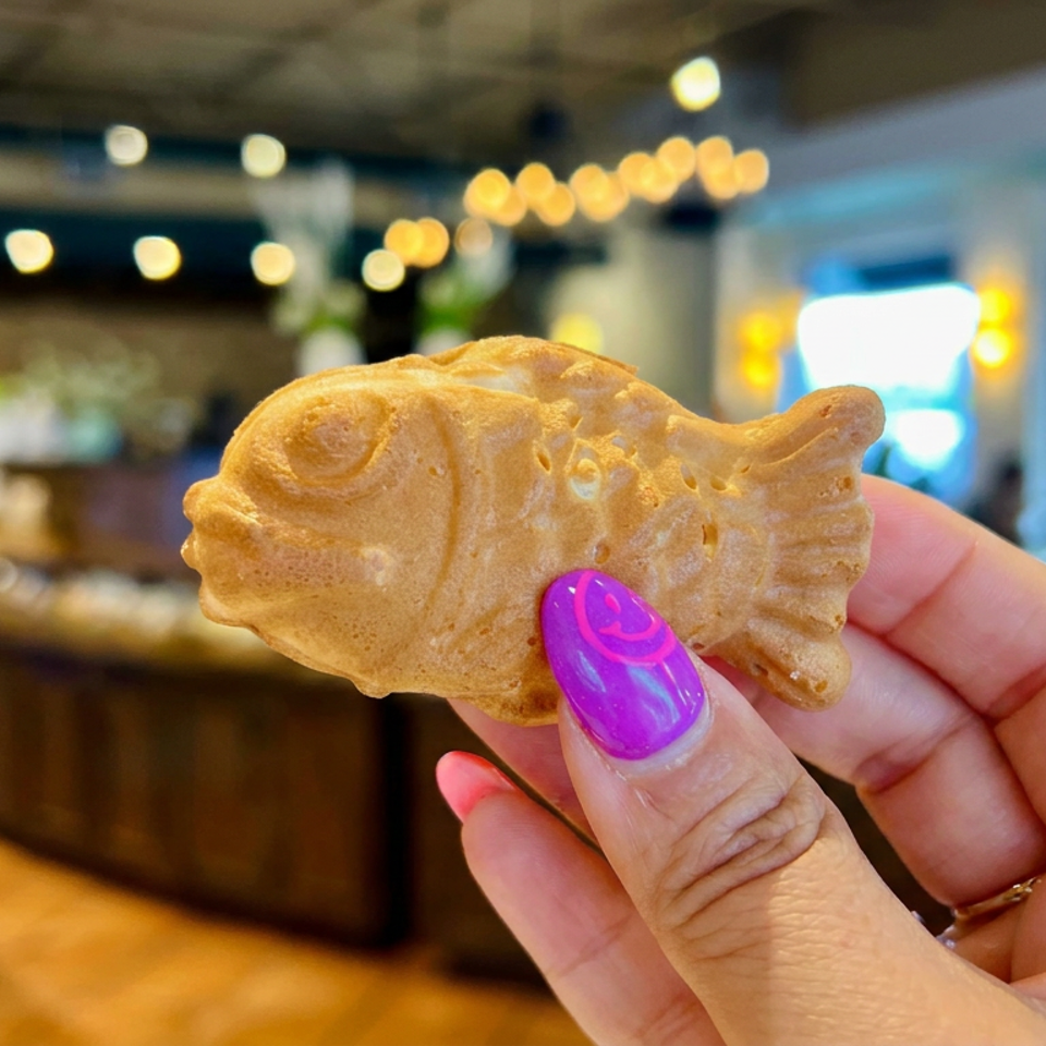 Hand holds a golden fish-shaped pastry inside a warmly lit restaurant.