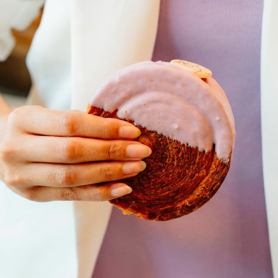 Person in an apron holds a round chocolate cake topped with pink frosting.