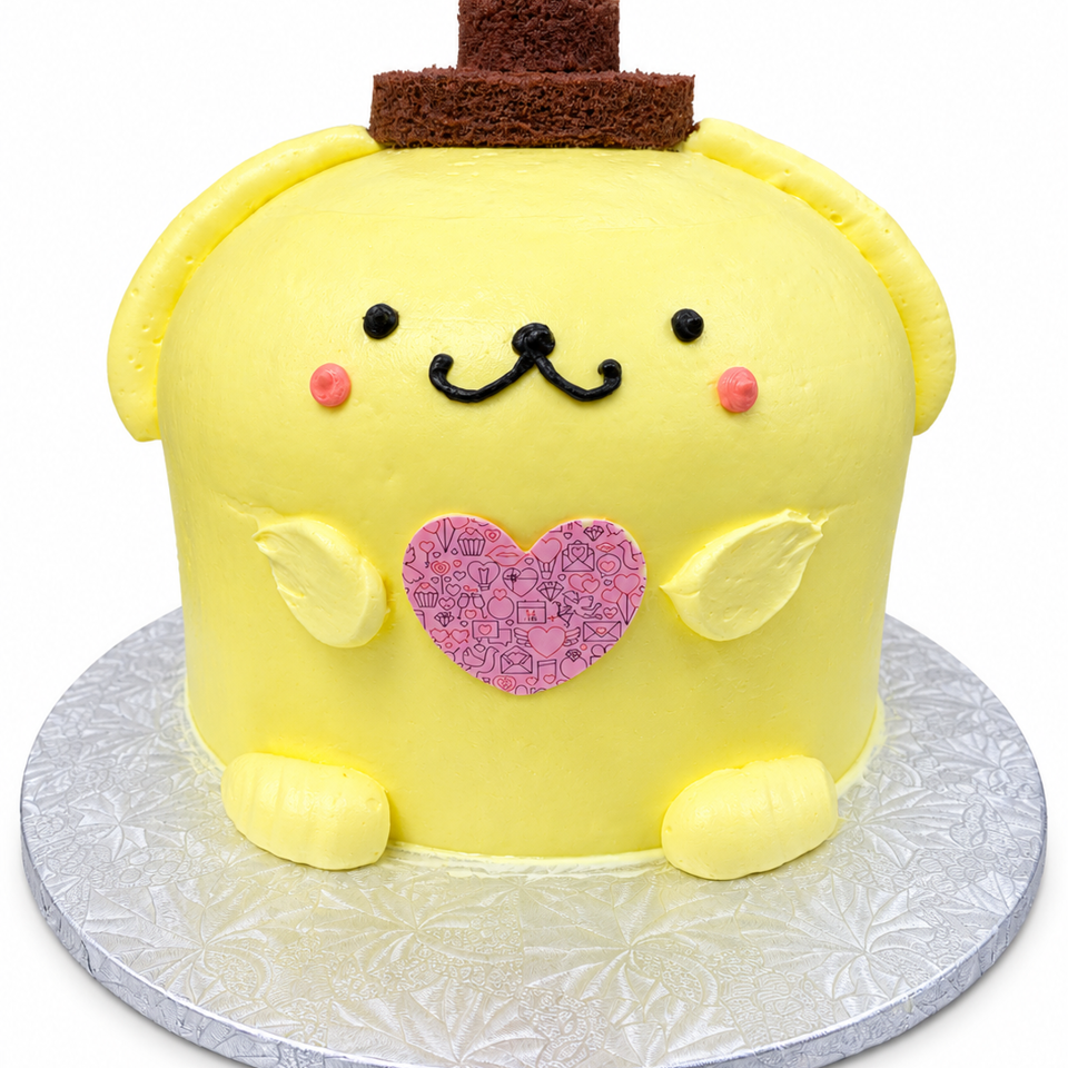 Yellow character-themed cake with chocolate hat, smiling face, pink patterned heart, and fondant hands and feet on a silver cake board.